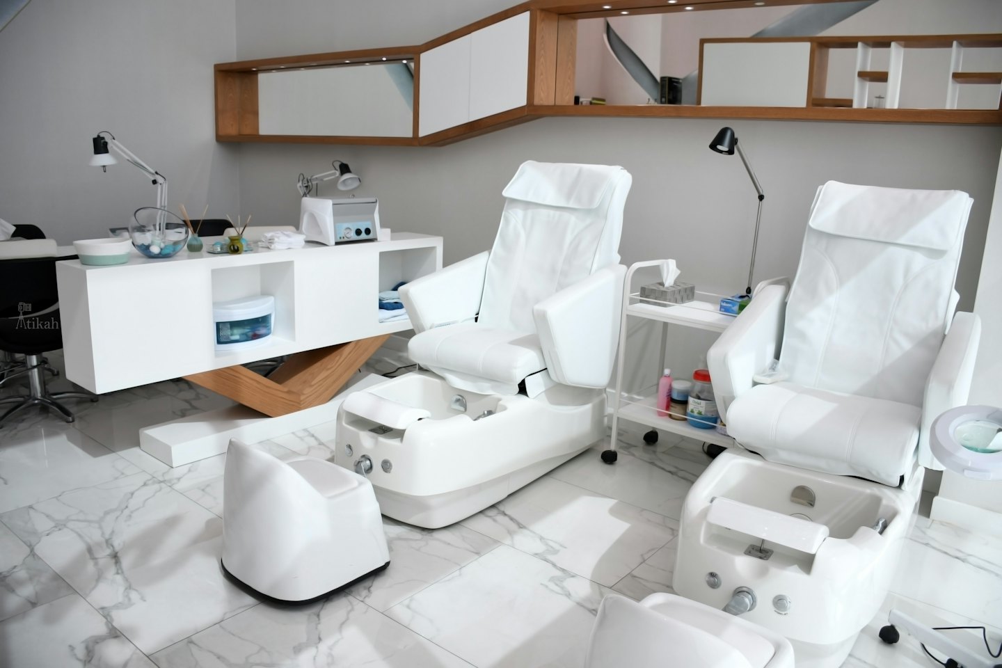 Two white spa pedicure chairs with foot baths in a modern salon.