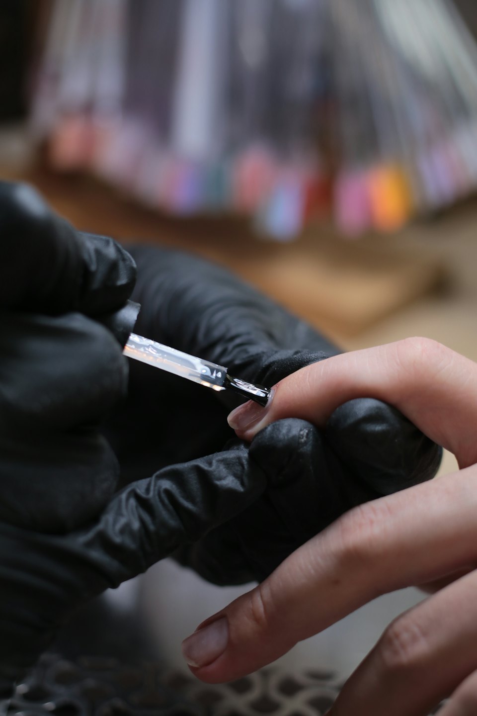 Manicurist in gloves applying clear polish to a client's nail.
