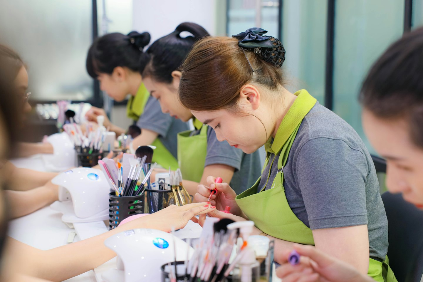 Nail technician applying pink polish to a client's fingernails.