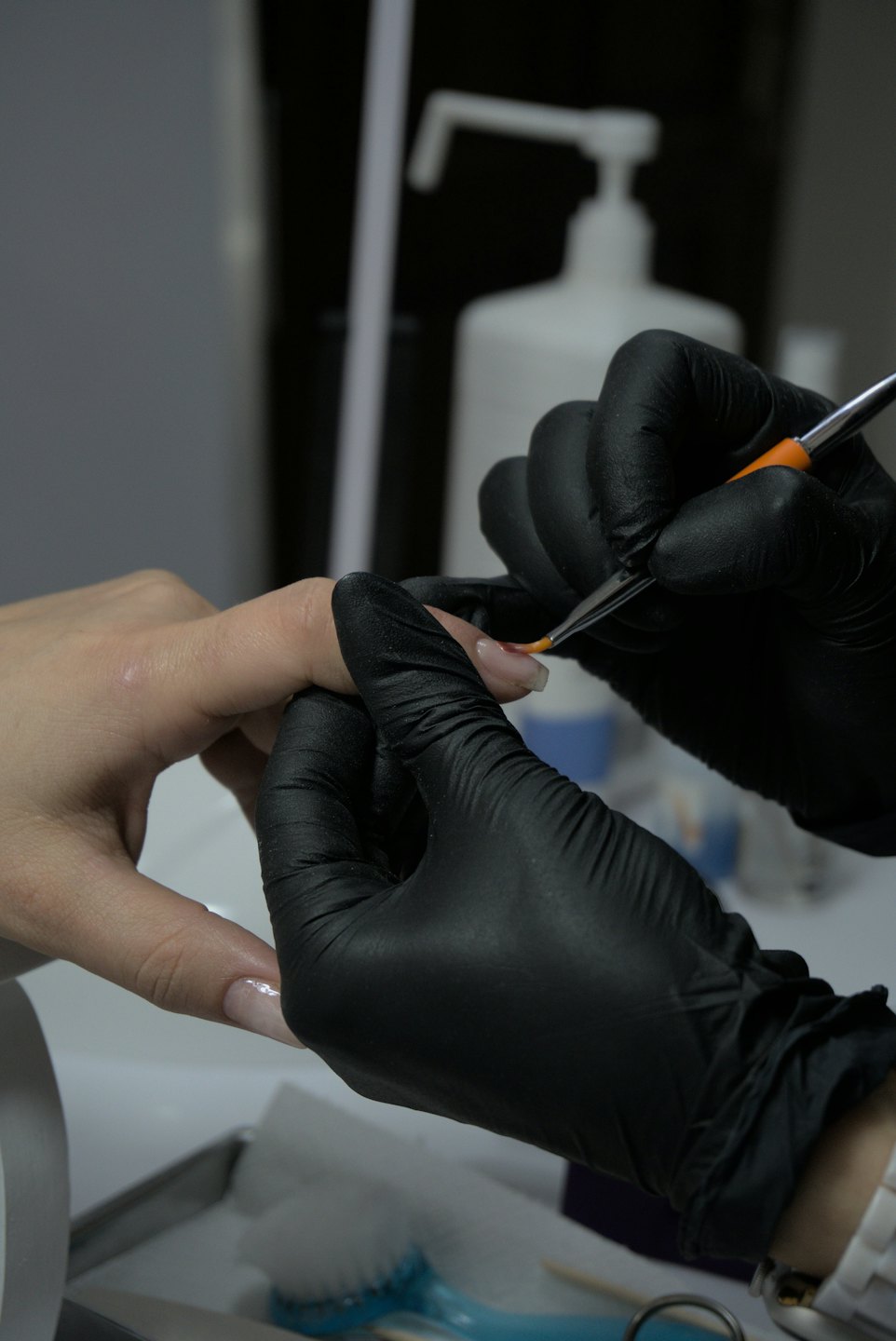 A nail technician paints a clear coat on a client's fingernail.